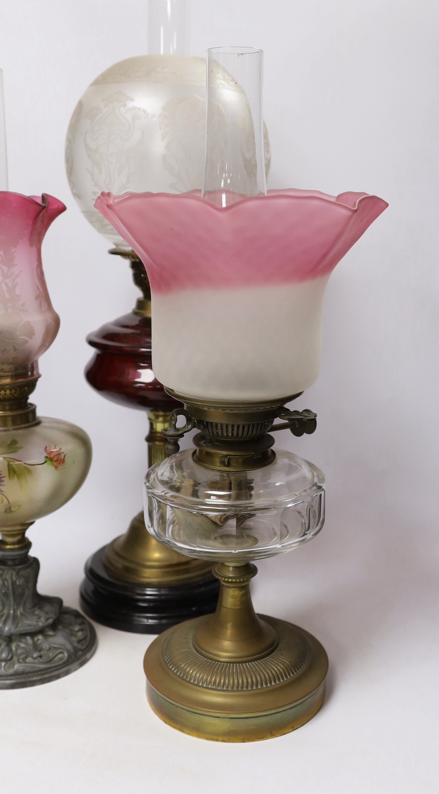 Three oil lamps with glass reservoirs and shades, one with Art Nouveau style base, 62cm high